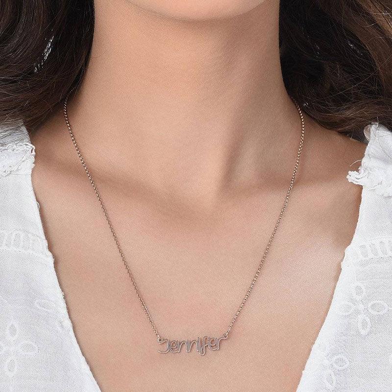 A woman wearing a delicate rose gold name necklace featuring the name “Jennifer,” styled with a simple chain and paired with a white blouse.