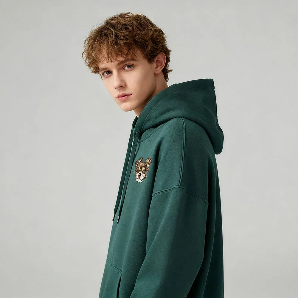 Person wearing a green embroidered hoodie on a light gray background