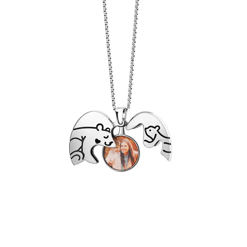 A silver necklace with two bear-shaped pendants forming a hugging design, holding a small photo of a smiling woman in the center.