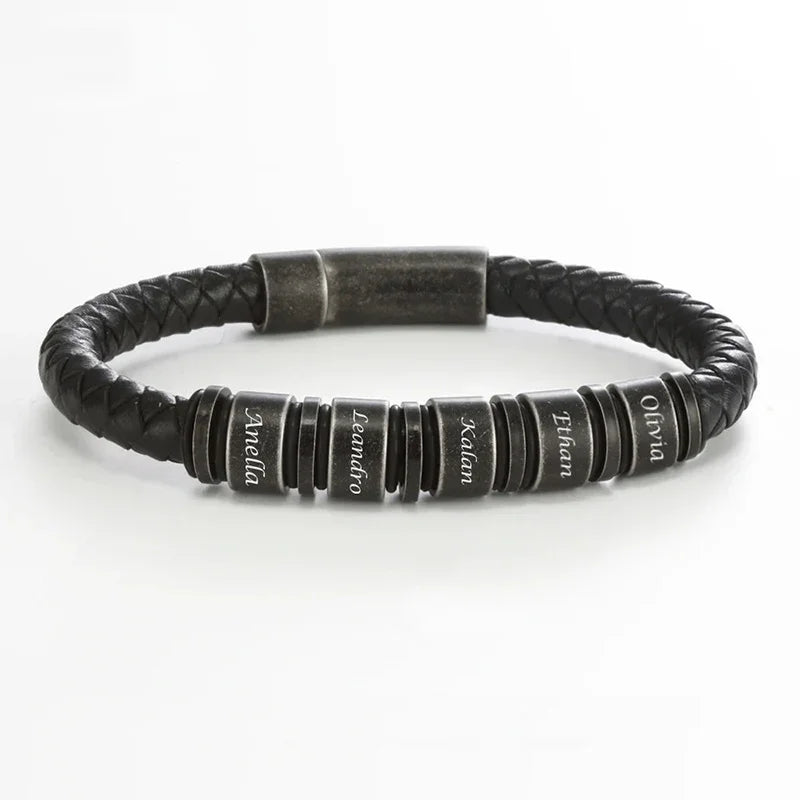 A men’s bracelet with a black braided leather strap and multiple round black beads evenly spaced along the band. Each bead features engraved lettering and is separated by thin metallic spacer rings. The bracelet has a sturdy magnetic clasp with a matte finish.