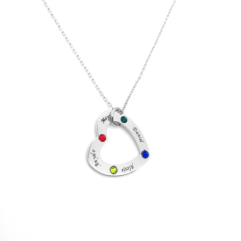 A silver heart-shaped necklace pendant with colorful gemstones and engraved names including Mayra, Daniel, and Alexis, displayed on a white background