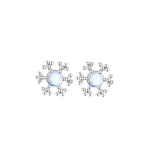 A pair of silver snowflake stud earrings featuring smooth, luminous round center stones. The elegant snowflake design radiates from the center, creating a festive and delicate winter look.