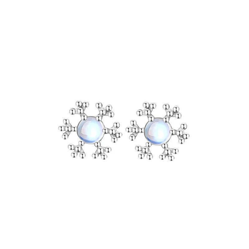 A pair of silver snowflake stud earrings featuring smooth, luminous round center stones. The elegant snowflake design radiates from the center, creating a festive and delicate winter look.