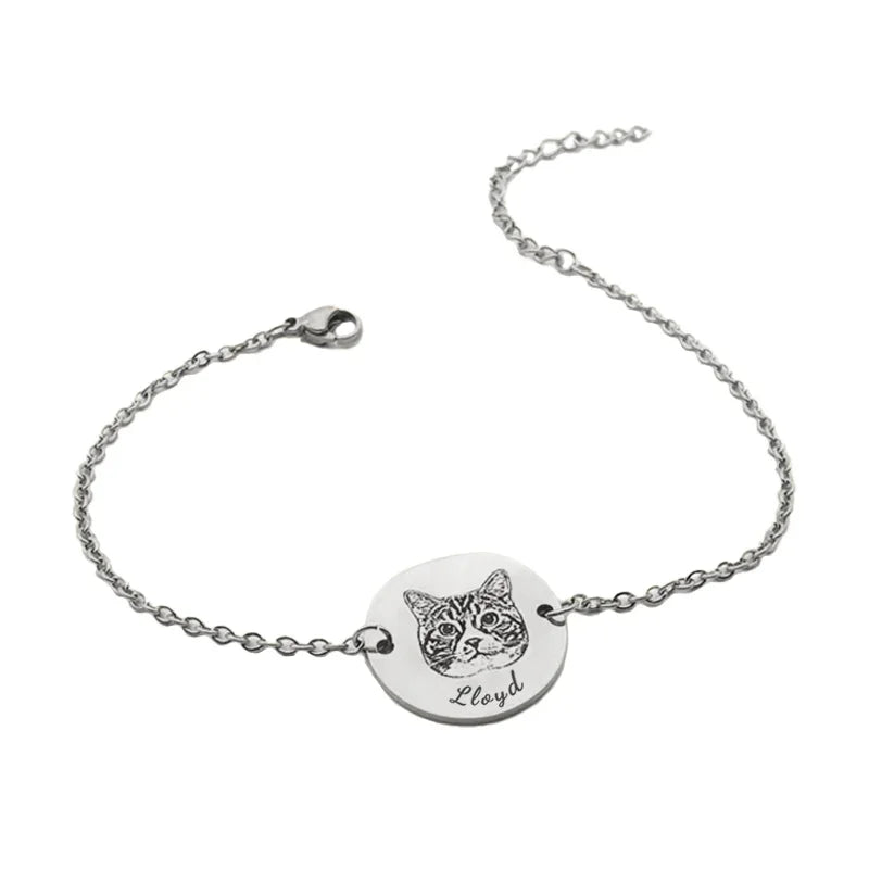 Silver bracelet with a round tag featuring a cat illustration and engraved text on a white background