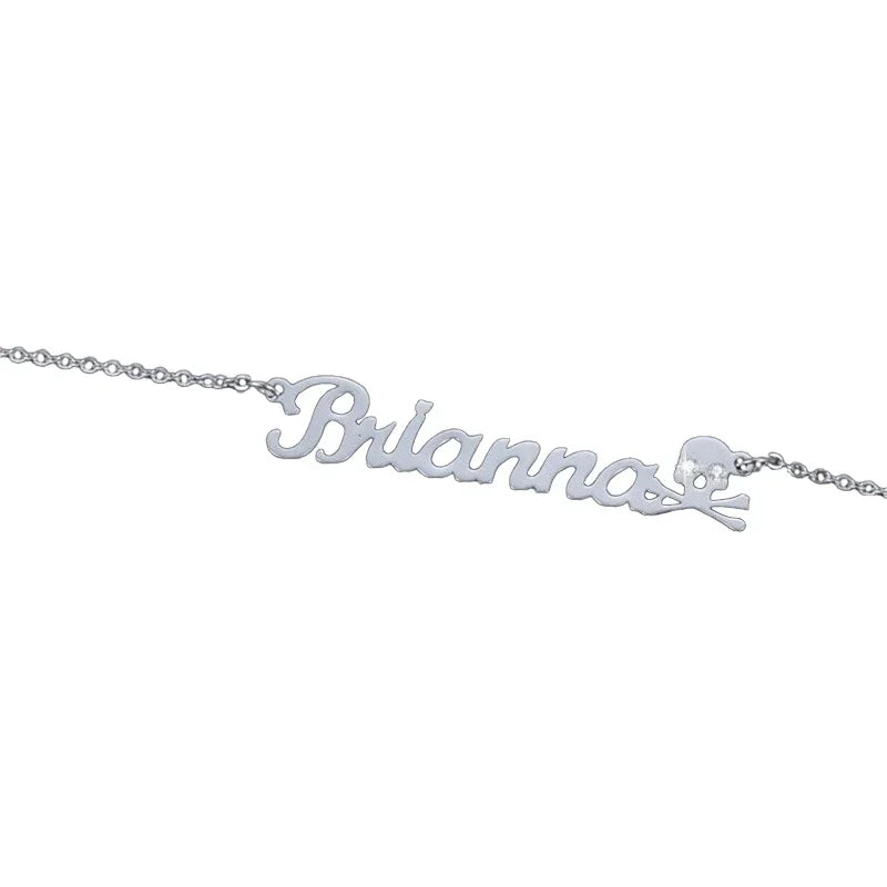 A personalized silver necklace featuring the name “Brianna” in elegant cursive script, accented with a small skull and crossbones charm at the end for a bold and stylish look.