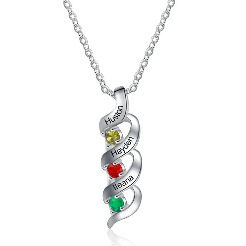 A personalized silver necklace featuring a twisting pendant with three engraved names — “Huston,” “Hayden,” and “Ileana” — each paired with a colorful gemstone in yellow, red, and green, symbolizing birthstones.