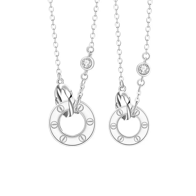 A pair of silver couple necklaces featuring interlocking circle pendants with engraved details and small sparkling gemstone accents, displayed on a white background.