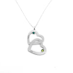 A silver necklace featuring two interlocking heart pendants, each engraved with a name and accented with a small green gemstone, symbolizing love and connection.