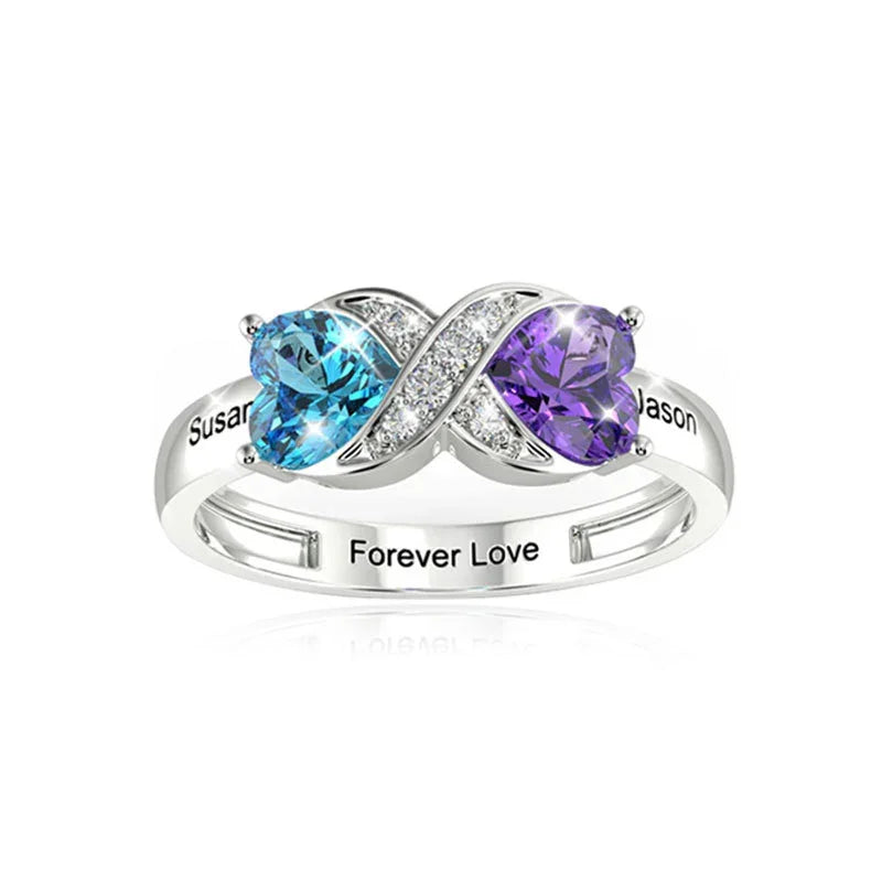 Silver infinity ring with blue and purple heart-shaped stones and engraved names.