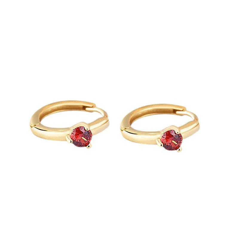 Gold hoop earrings with red birthstones on a white background