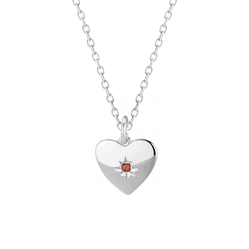 Silver heart-shaped pendant with a red gemstone on a white background