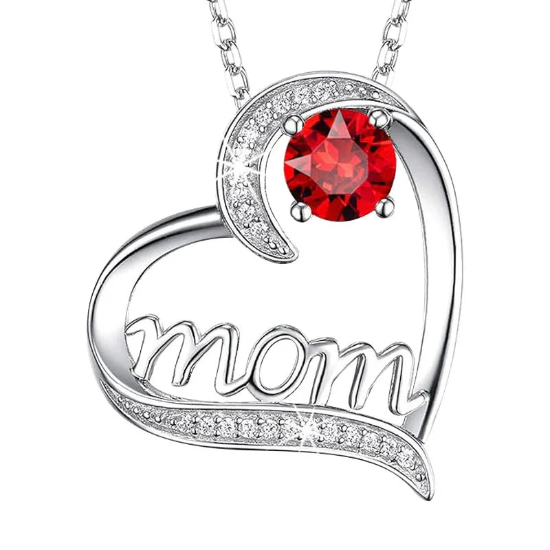 Silver heart-shaped pendant featuring the word “Mom” inside the design, accented with a crescent shape and a central red round gemstone, displayed on a white background.