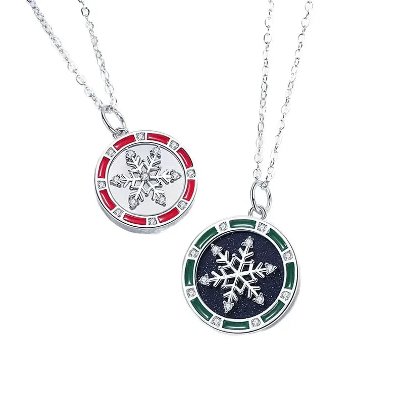 A pair of matching silver couple necklaces featuring round pendants with snowflake designs — one with a black background and green border, and the other with a white background and red border, both accented with small crystals, displayed on a white background.