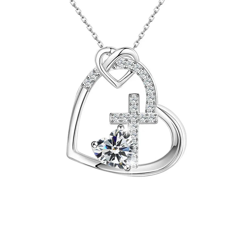 Silver heart-shaped pendant featuring a cross and a central heart-shaped gemstone adorned with small sparkling crystals, displayed on a white background.