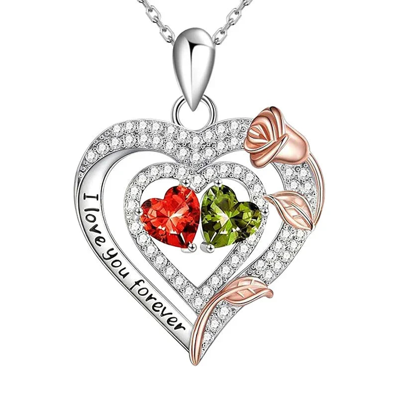 Heart-shaped pendant with 'I love you forever' engraving, red and green gemstones, and rose gold accents on a white background.