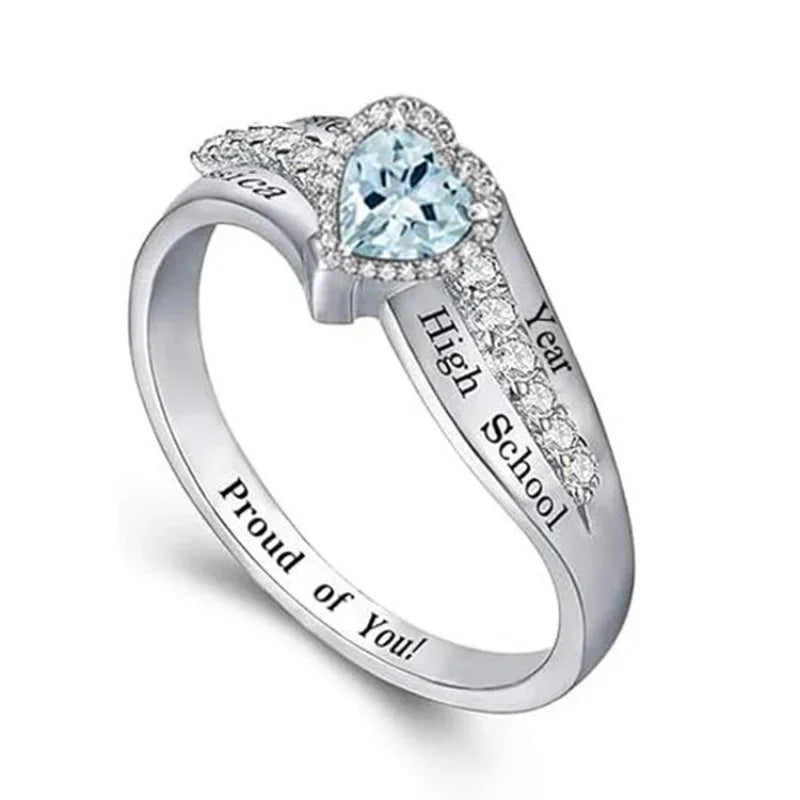 Silver ring with a light blue heart-shaped stone and engraved graduation-style text.