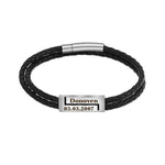A black braided leather bracelet with a rectangular silver nameplate featuring engraved text, secured with a sleek metallic clasp.