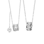 A pair of sterling silver couple necklaces with cylinder pendants. The women’s necklace features a sparkling silver cylinder with clear stones and a delicate rose charm, while the men’s necklace has a matching cylinder with black stone accents. Both are displayed on fine silver chains against a white background.