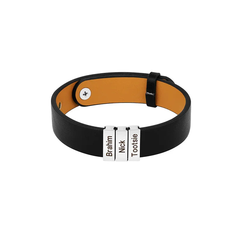 A men’s black leather bracelet featuring three customizable stainless steel name plates engraved with “Brahim,” “Nick,” and “Tootsie.” The bracelet has a simple and sleek design with an adjustable buckle closure and a contrasting tan inner lining.