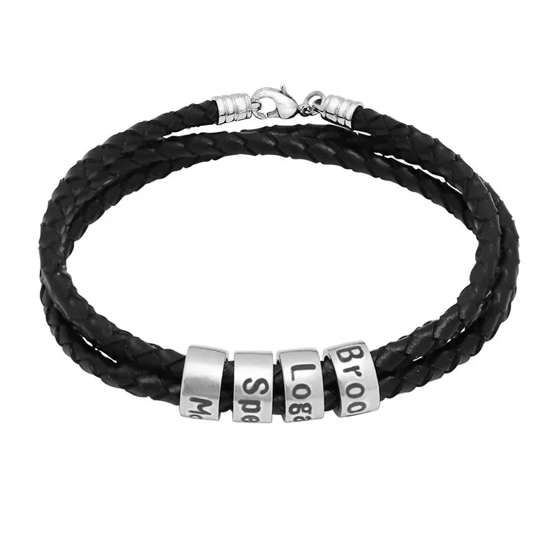 A men's black braided leather bracelet with multiple stainless steel name rings engraved with different names. The bracelet features a lobster clasp closure and a sleek, modern design, symbolizing personal connection and style.