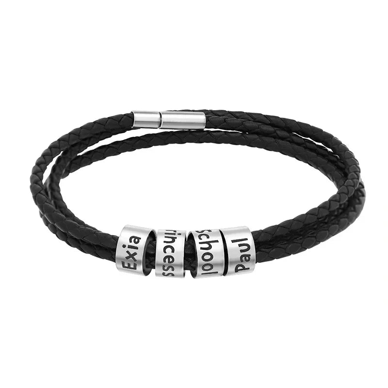 A men's black braided leather bracelet featuring multiple stainless steel name rings engraved with custom text. The bracelet has a sleek, modern design with a secure magnetic clasp, symbolizing personalization and style.