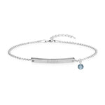 Silver bracelet with a thin chain, engraved bar reading “EMMA,” and a small blue birthstone charm.