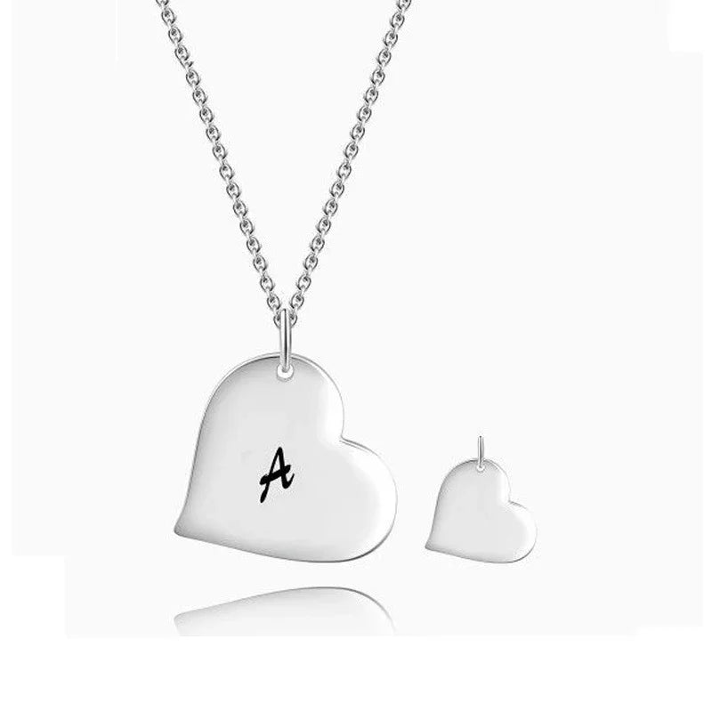 A minimalist silver heart-shaped pendant necklace featuring a single engraved letter “A” on the larger pendant, paired with a smaller matching heart charm, displayed against a clean white background.