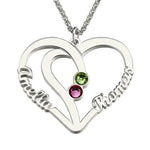 A silver heart-shaped necklace pendant featuring two engraved names, “Amelia” and “Thomas,” with two colorful birthstones — one green and one pink — set in the center, symbolizing love and connection.