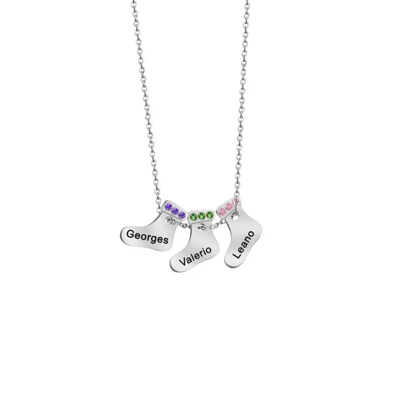 A silver necklace featuring three Christmas stocking charms, each engraved with a name and adorned with colorful birthstones along the top edges.