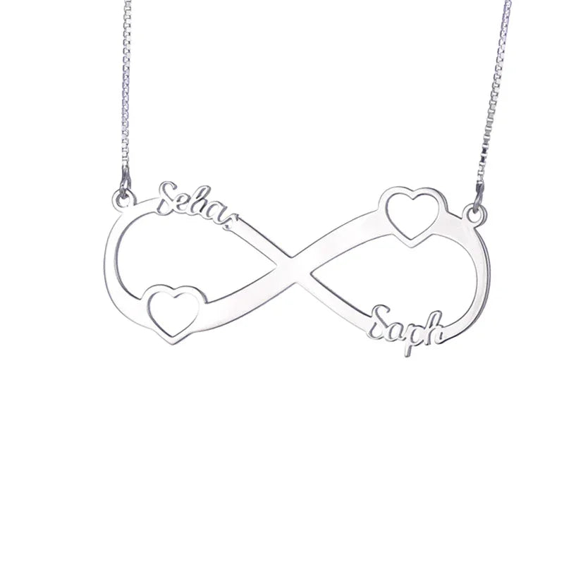 A silver infinity necklace with two small heart shapes incorporated into the design and engraved names “Selas” and “Saph” on each side. The pendant is attached to a fine silver chain, symbolizing eternal love and connection.