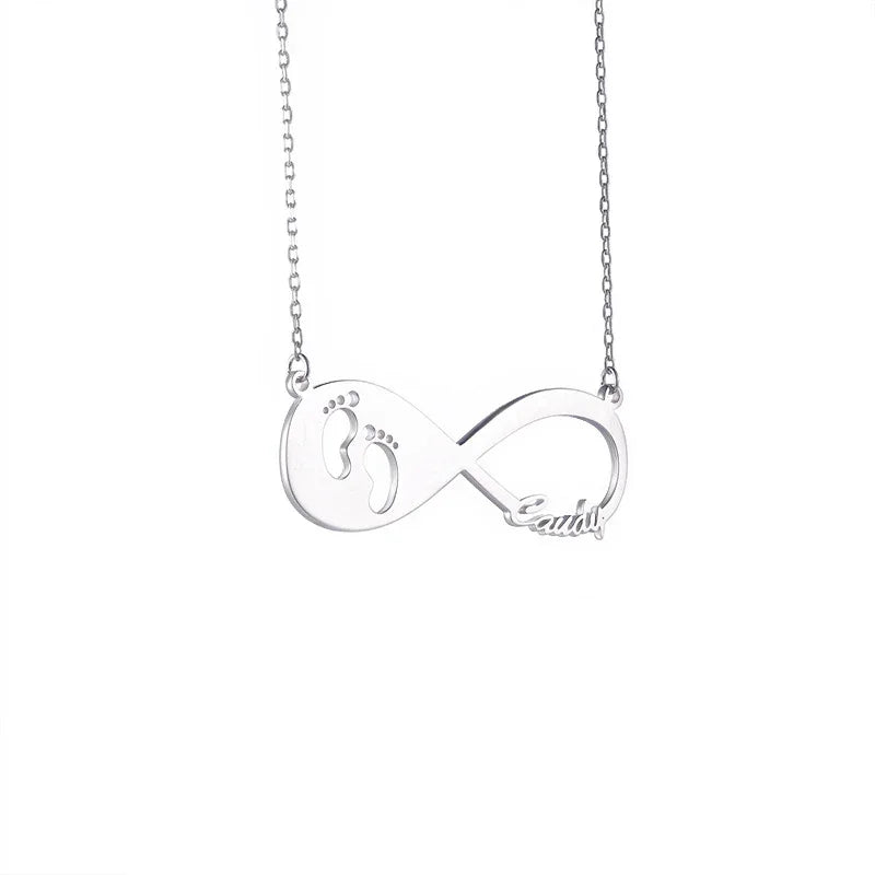 A silver infinity necklace with a delicate pendant featuring baby footprint cutouts on one side and a customized name “Candy” on the other. The pendant is attached to a fine silver chain, symbolizing love and connection.