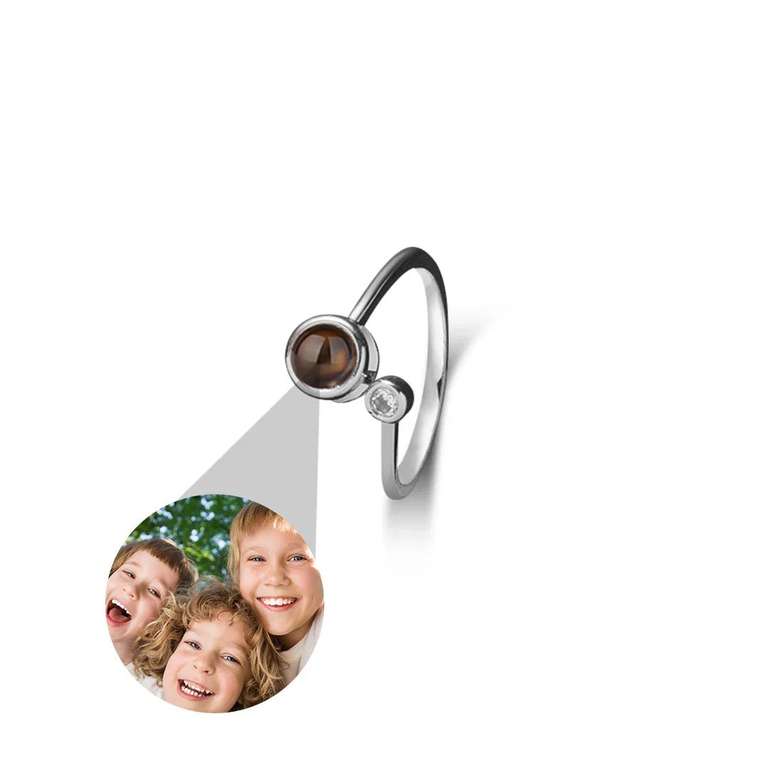Silver ring with a brown gemstone and diamond, projected onto a white background with a photo of two children.