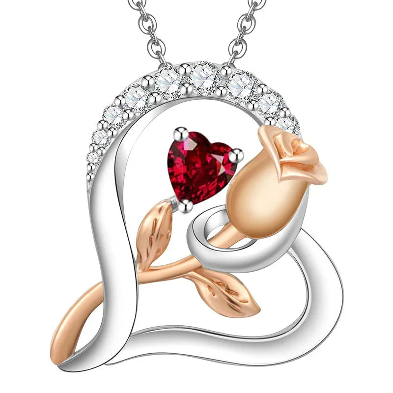 Silver heart-shaped pendant featuring a rose design with gold accents and a central red heart-shaped gemstone, adorned with sparkling crystals on a white background.