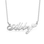 A silver personalized name necklace featuring the name “Abby” in elegant cursive script, with a small heart accent at the end of the name. 