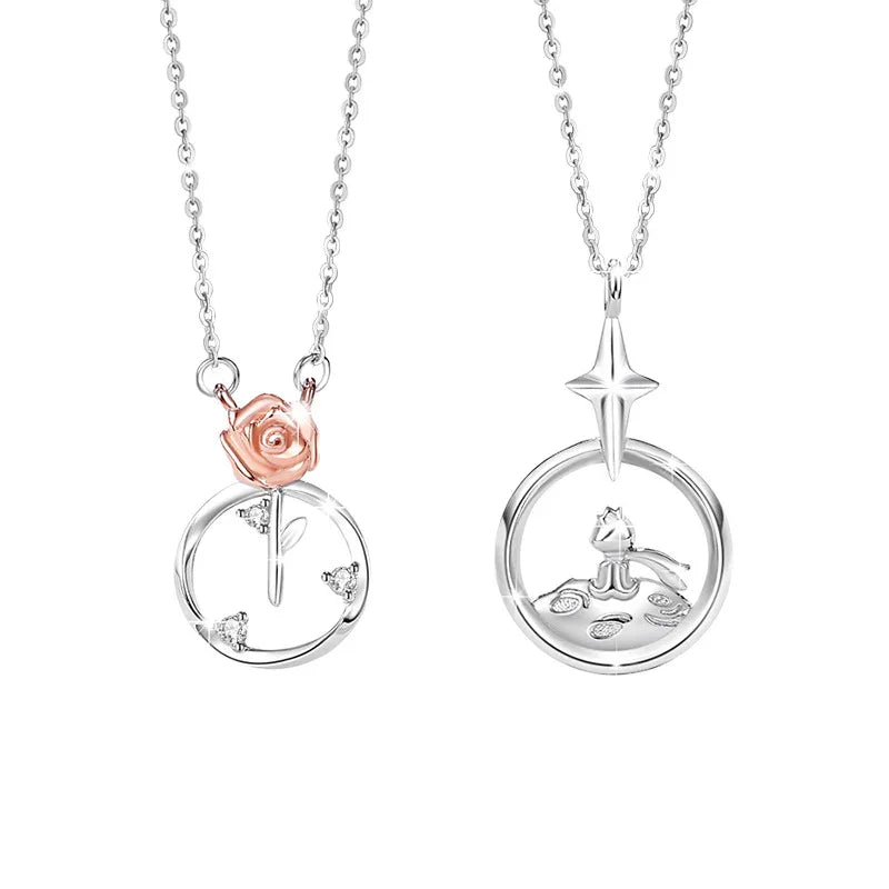 A pair of sterling silver couple necklaces. One pendant features a delicate rose with sparkling accents inside a circular frame, while the other shows a little prince figure sitting on a small planet beneath a star. Both are displayed on fine silver chains against a white background.