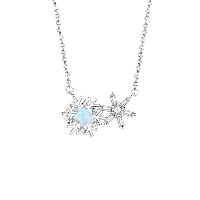 A delicate silver necklace featuring two connected snowflake pendants — one with an iridescent star-shaped center and the other with a sparkling crystal centerpiece, displayed on a white background.