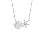 A delicate silver necklace featuring two connected snowflake pendants — one with an iridescent star-shaped center and the other with a sparkling crystal centerpiece, displayed on a white background.