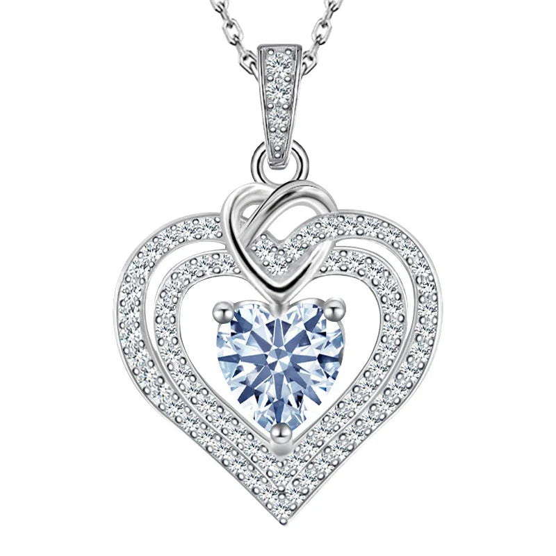 Heart-shaped silver pendant with a central blue gemstone on a white background