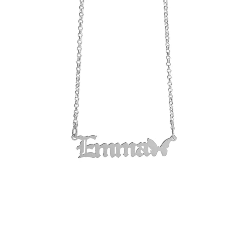 A customized silver name necklace featuring the word “Emma” in bold Old English-style lettering, with a delicate butterfly silhouette attached at the end, symbolizing elegance and transformation.