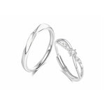 A pair of elegant silver couple rings displayed on a white background. One ring features a smooth, twisted band with a minimalist design, while the other has a delicate crisscross shape adorned with small sparkling gemstones, symbolizing love and unity.